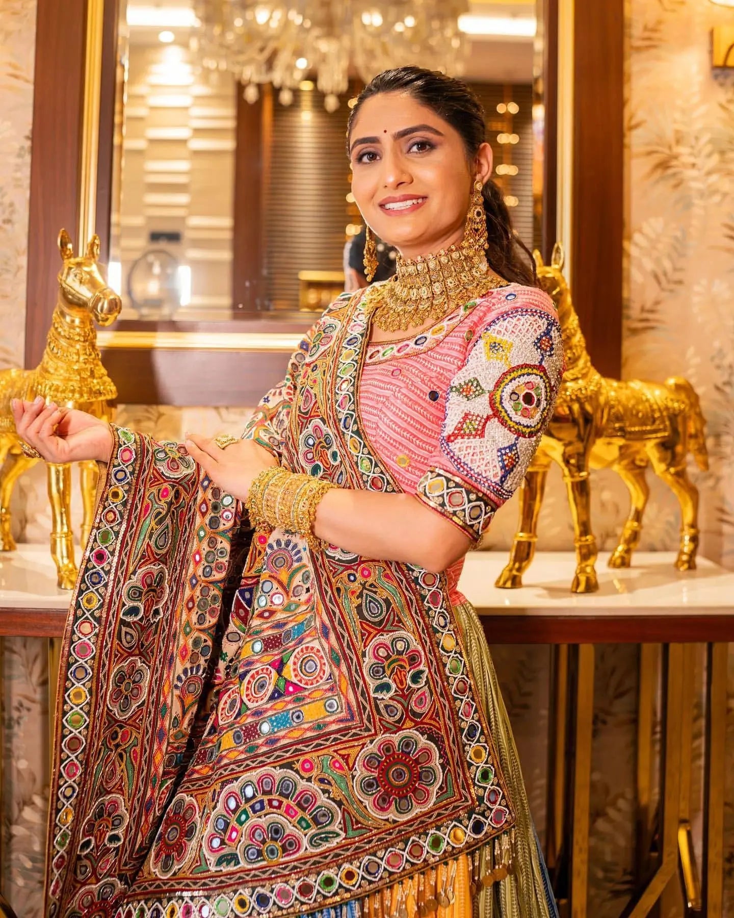 Woman in traditional embroidered outfit with gold jewelry in a decorated interior setting